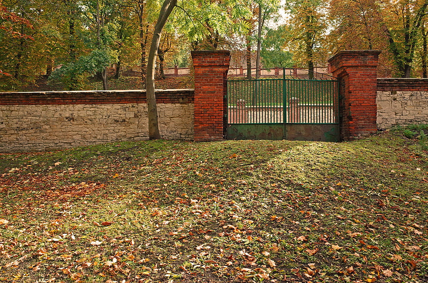 Autumn park entrance with brick wall and green metal gate
