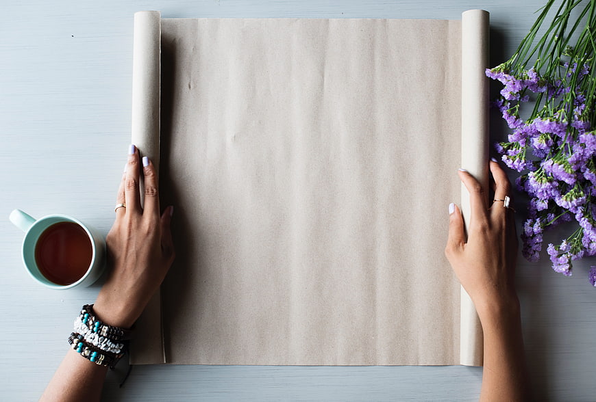 Flat lay of hands holding blank paper with coffee and purple flowers