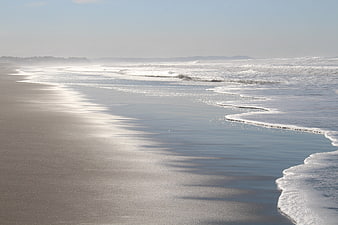 Serene Sandy Beach with Gentle Waves and Misty Horizon