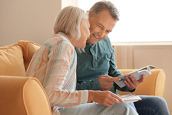 Happy senior couple reading magazine on sofa at home