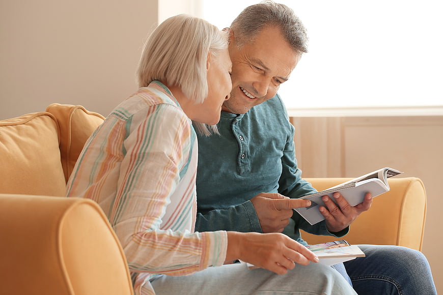 Happy senior couple reading magazine on sofa at home