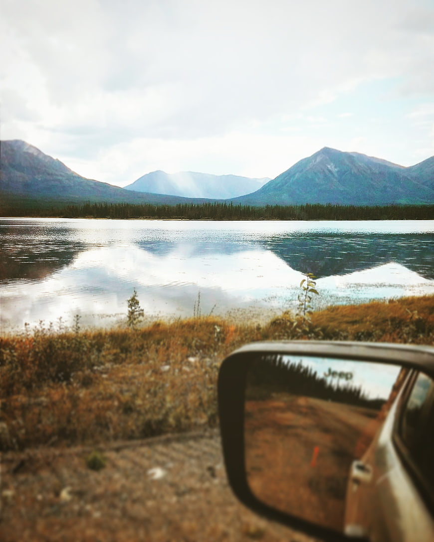 Jeep side mirror reflecting lake and mountain landscape
