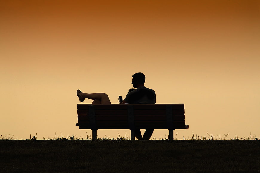Silhouette of couple relaxing on park bench at sunset
