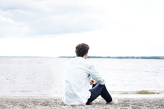Man sitting alone on beach looking at ocean