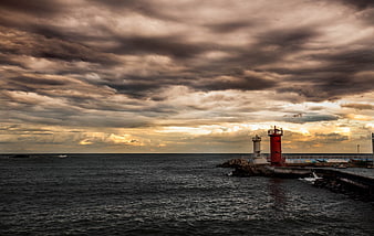 Dramatic sunset over ocean with red lighthouse and stormy clouds