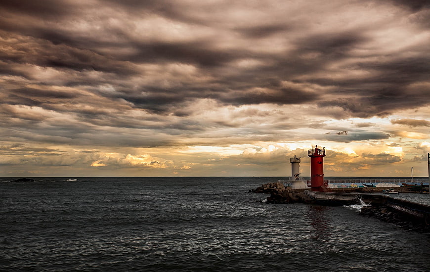 Dramatic sunset over ocean with red lighthouse and stormy clouds