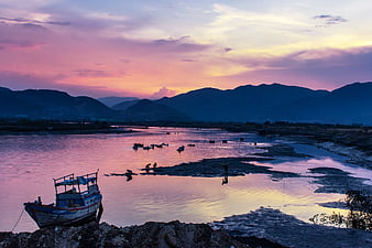 Fishing boat on riverbank at sunset with mountains