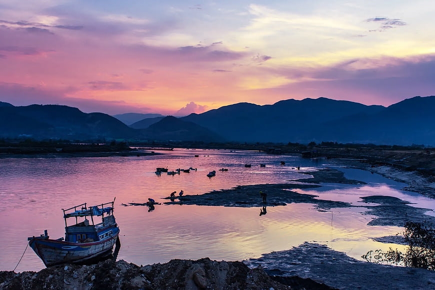 Fishing boat on riverbank at sunset with mountains