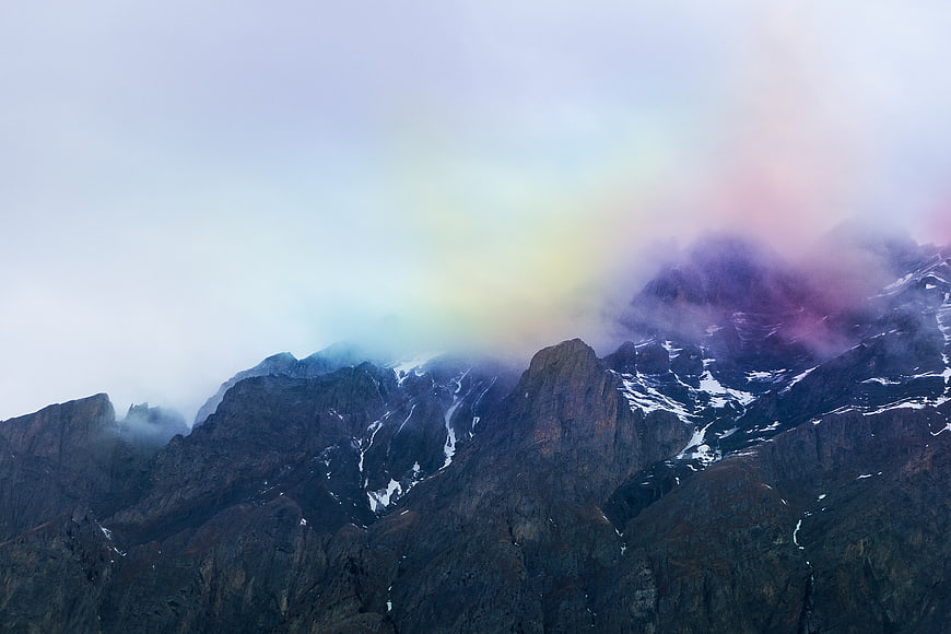 Majestic mountain peaks with pastel rainbow clouds and snow