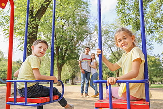 Happy children on swings with parents in background