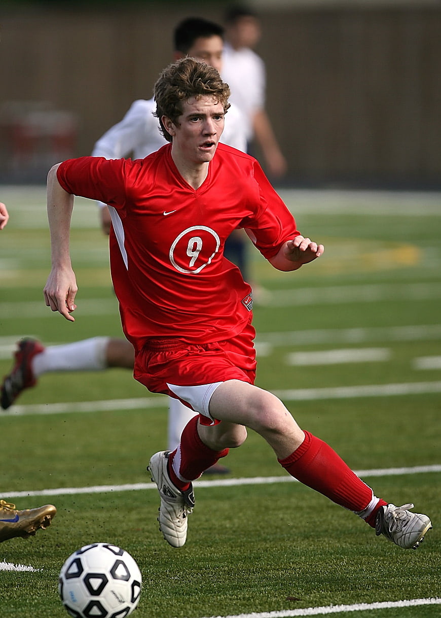 Young soccer player in red uniform kicking ball on grass field