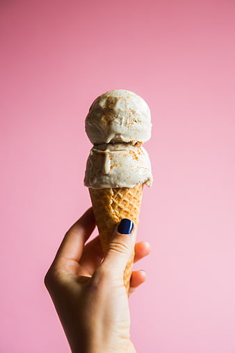Hand holding double scoop ice cream cone on pink background