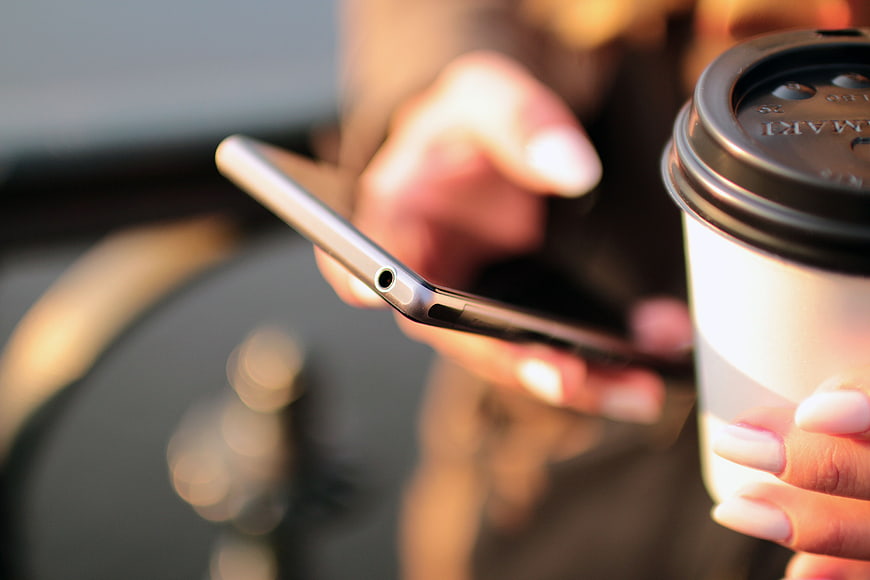 Close-up of woman holding smartphone and coffee cup