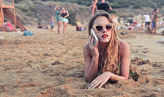 Woman with sunglasses talking on phone at sandy beach