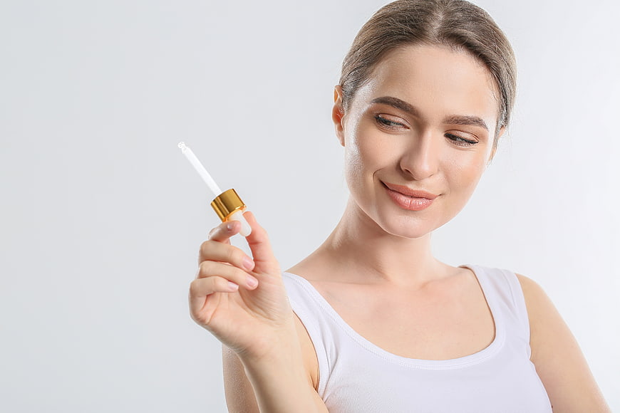 Woman holding skincare serum dropper with copy space