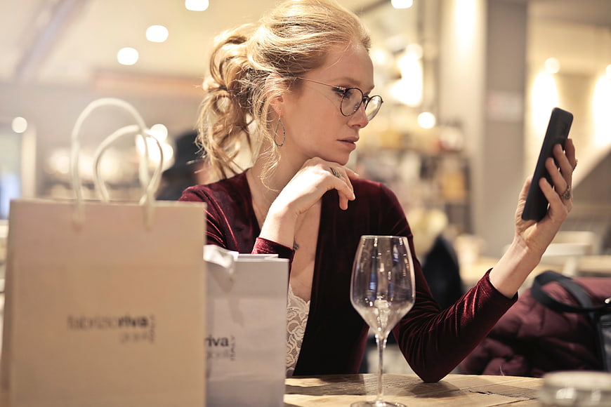 Woman with glasses checking phone at cafe with shopping bags