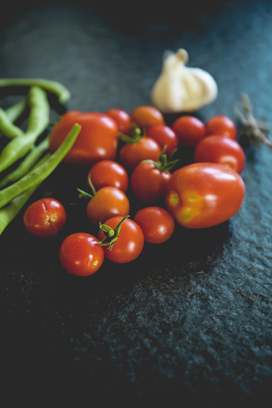 Fresh tomatoes, green beans, and garlic on dark slate background