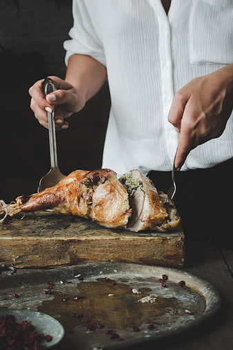 Woman carving roasted turkey thigh on rustic wooden board