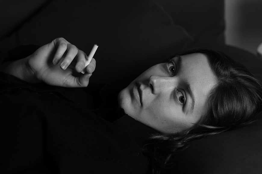 Black and white portrait of a woman lying down holding a cigarette