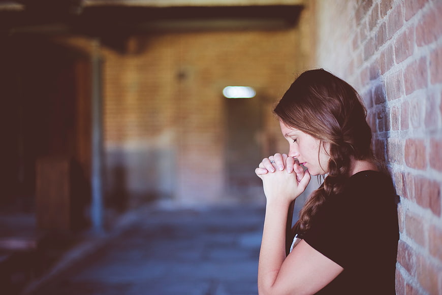 Young woman praying against brick wall in church