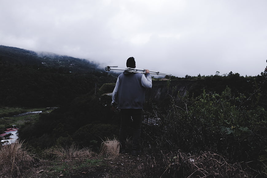 Man carrying tripod on misty mountain ridge