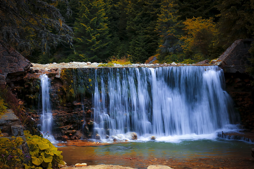 Serene Waterfall Cascading Over Stone Dam in Autumn Forest