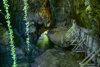 Wooden walkway through mossy cave with emerald river
