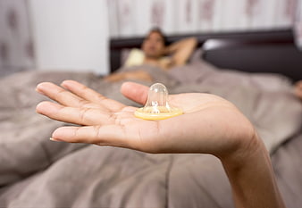 Woman holding condom in hand with blurred bedroom background