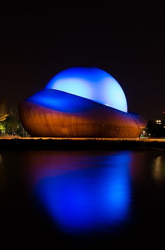 Infoversum Groningen illuminated at night with blue and orange lights reflecting in water