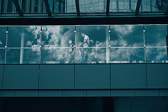 People walking on glass skybridge with cloud reflection