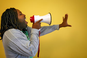 Man with dreadlocks shouting into megaphone on yellow background