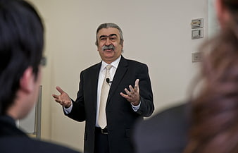 Senior male speaker presenting to audience in business suit