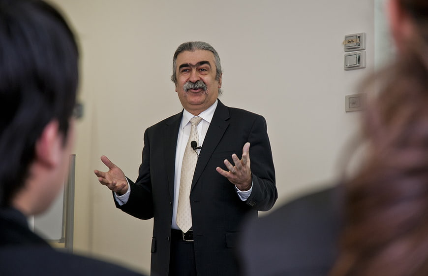 Senior male speaker presenting to audience in business suit