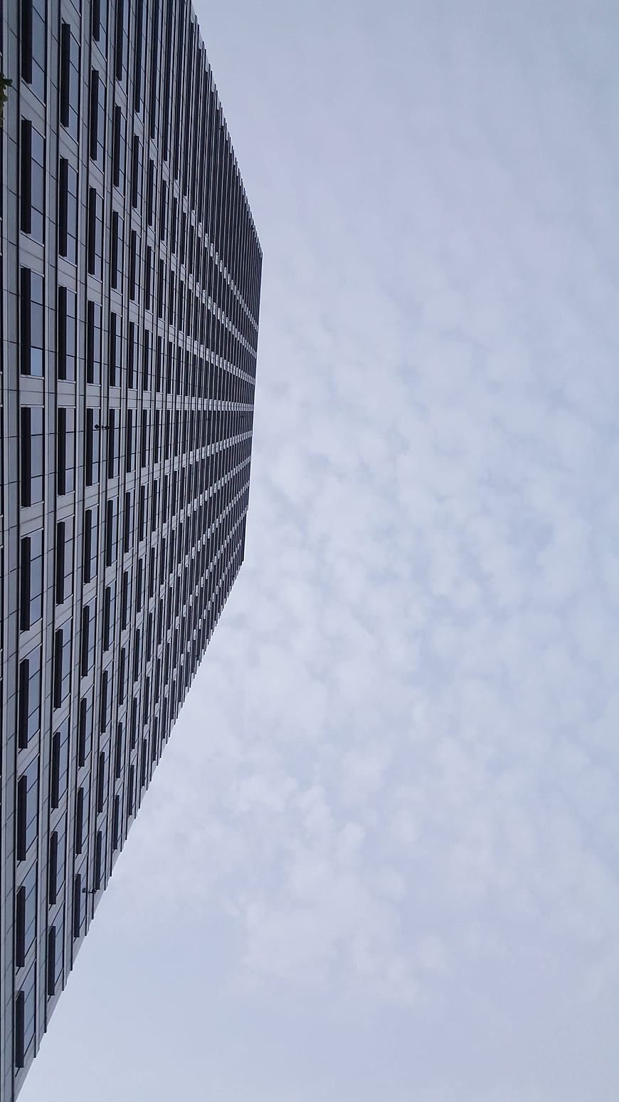 Low angle view of modern skyscraper against cloudy sky