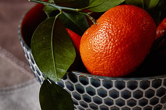 Close-up of fresh tangerines with green leaves in a patterned ceramic bowl