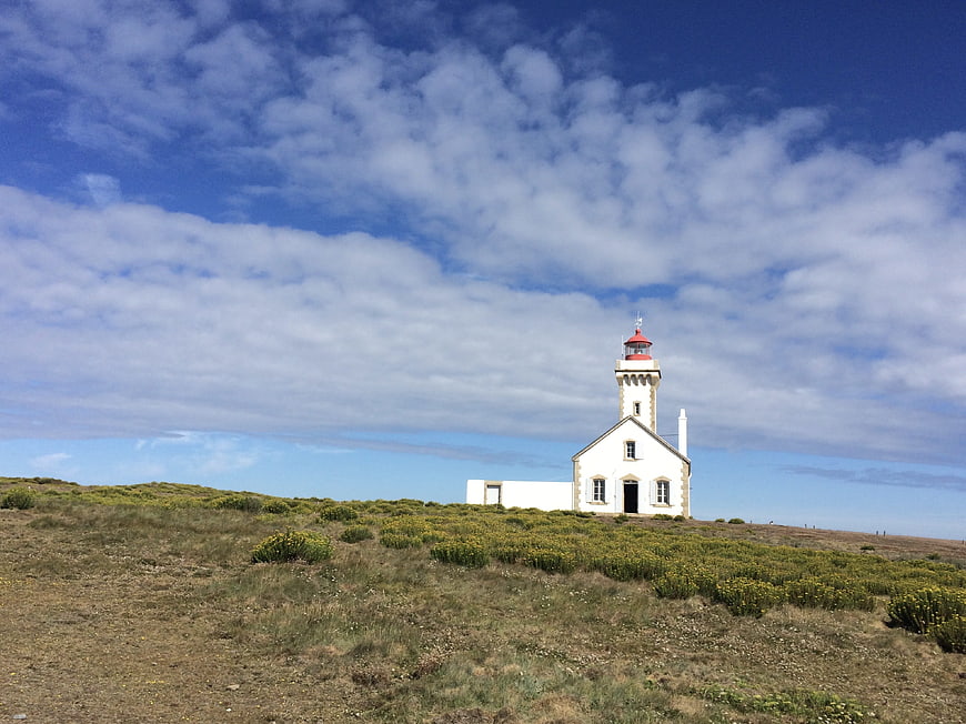 White Lighthouse Building On Grassy Hill Under Blue Sky