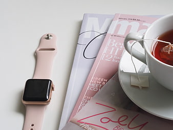 Pink Apple Watch, Magazines, and Cup of Tea on White Surface