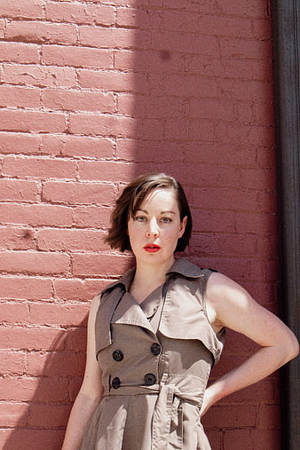 Woman in beige dress posing against pink brick wall