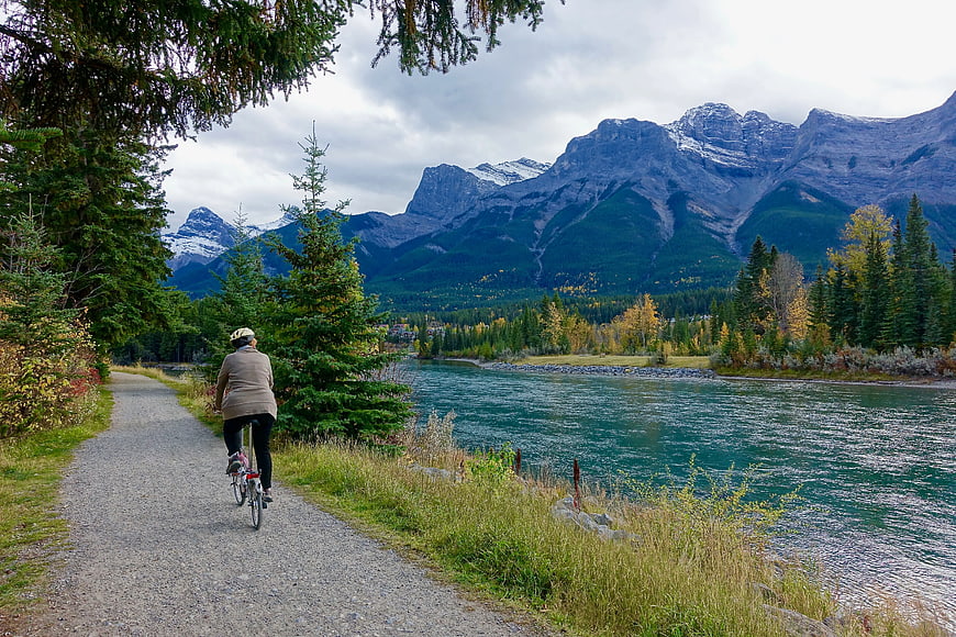 Woman Cycling on Gravel Path by River and Mountains