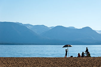 Family relaxing on sandy beach with mountains and lake