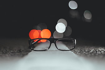 Black eyeglasses on asphalt road with night bokeh lights