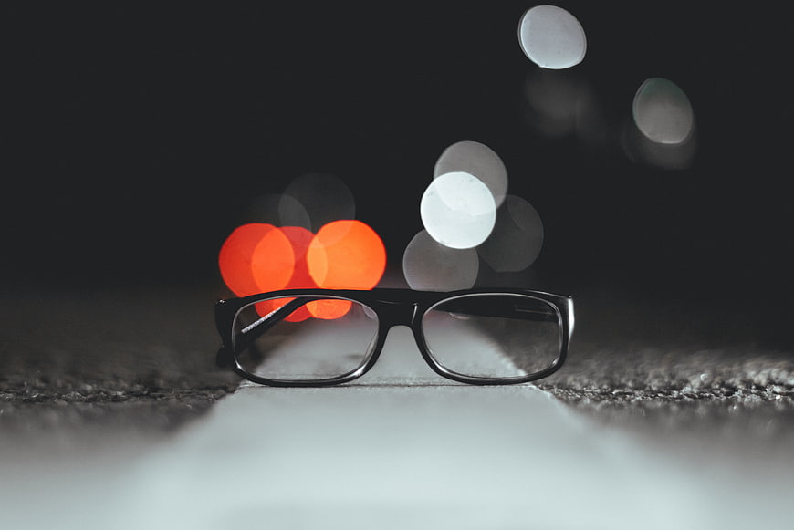 Black eyeglasses on asphalt road with night bokeh lights