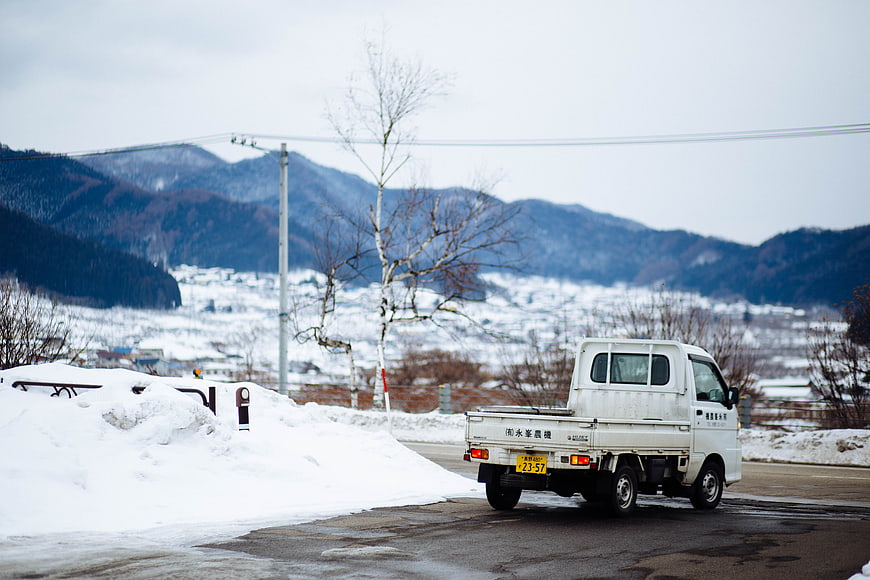 White pickup truck driving on snowy mountain road in winter