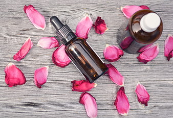 Amber essential oil bottles with pink rose petals on wood