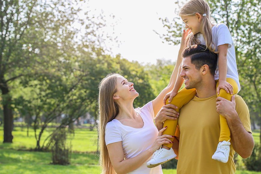 Happy family with daughter on father's shoulders in park