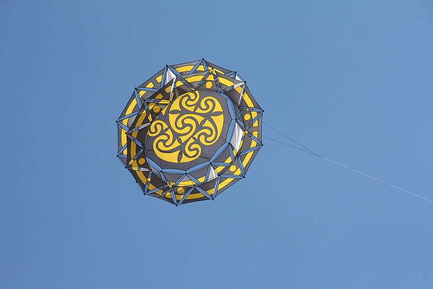 Geometric yellow and black kite flying in blue sky