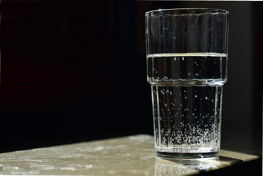Glass of sparkling water with bubbles on a dark background