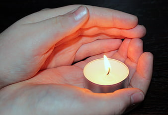Hands cupping a lit tea light candle in the dark