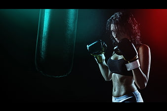 Female Boxer Training with Punching Bag in Dark Gym