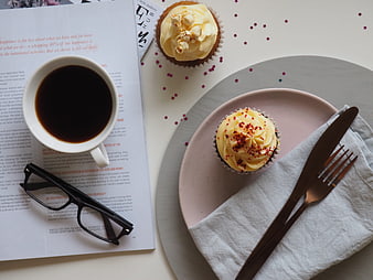 Flat lay of coffee, cupcakes, and reading glasses on a white table